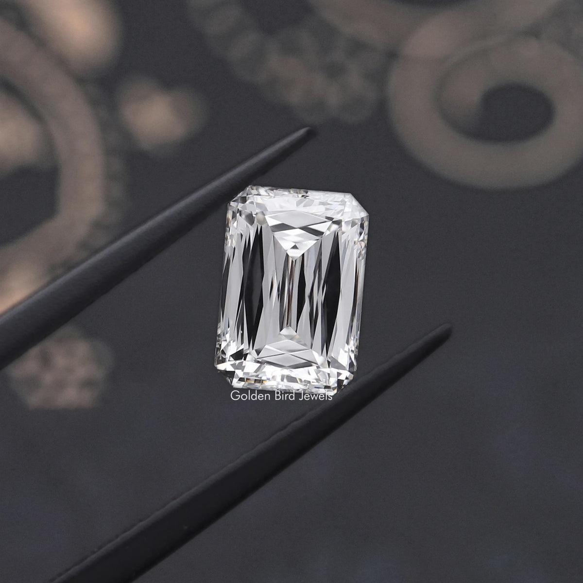 Rectangular emerald-cut lab-grown diamond held in tweezers, step facets visible