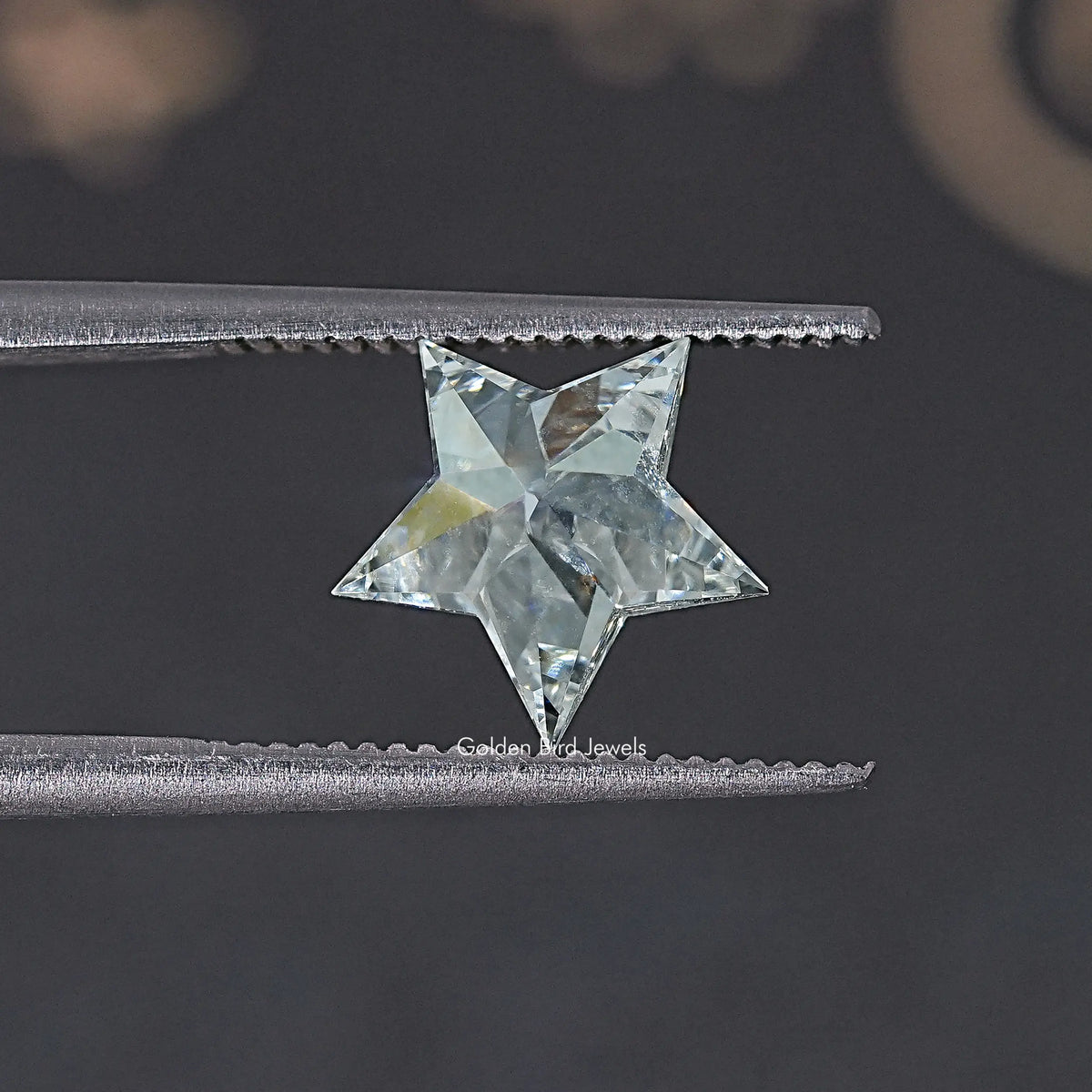 Star-cut lab diamond with clear, faceted sparkle, held between metal tweezers