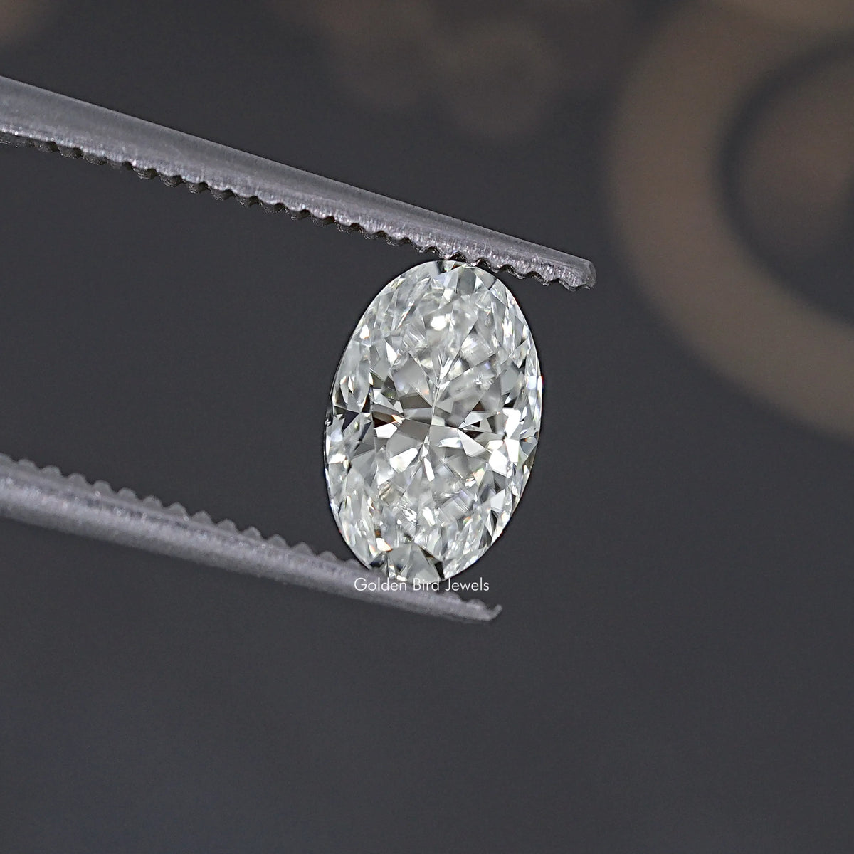 Oval clear moissanite gemstone with crisp facets between gray tweezers