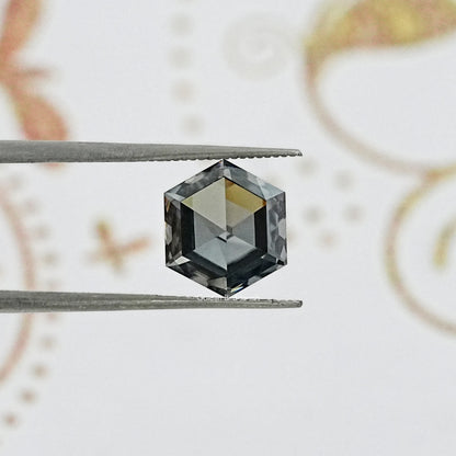 Hexagon-cut gray moissanite gemstone between tweezers, faceted reflective surfaces