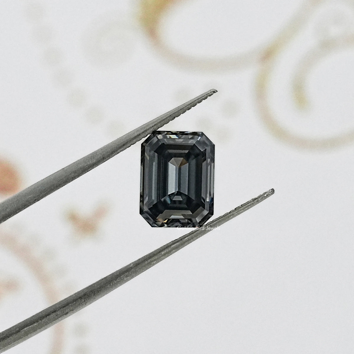 Gray emerald-cut gemstone held in tweezers, angled view