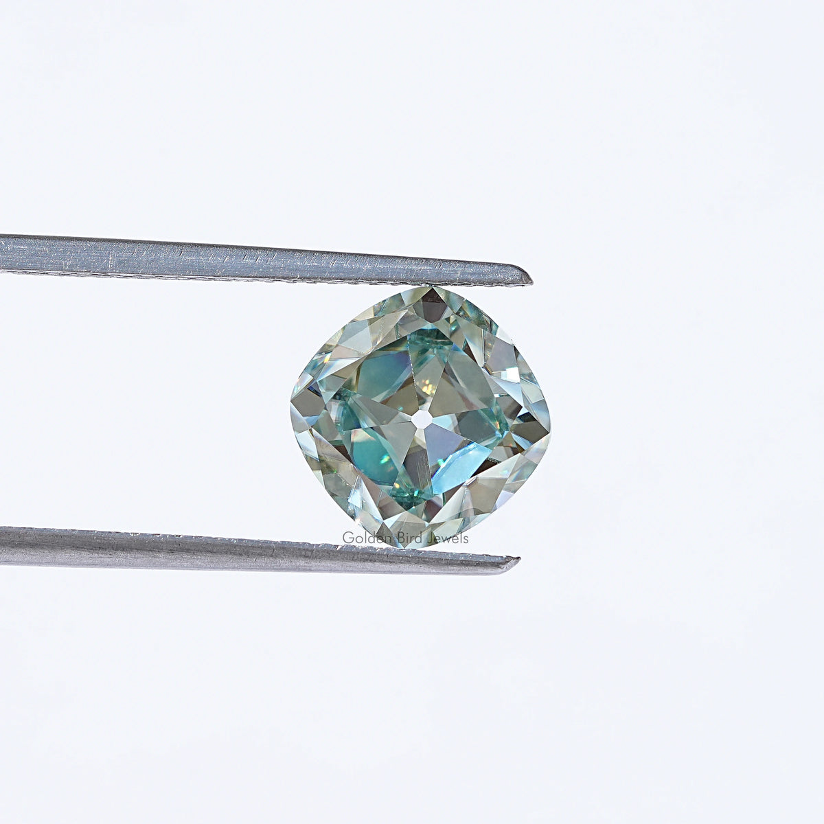 Light blue moissanite gemstone in silver tweezers, cushion old mine cut
