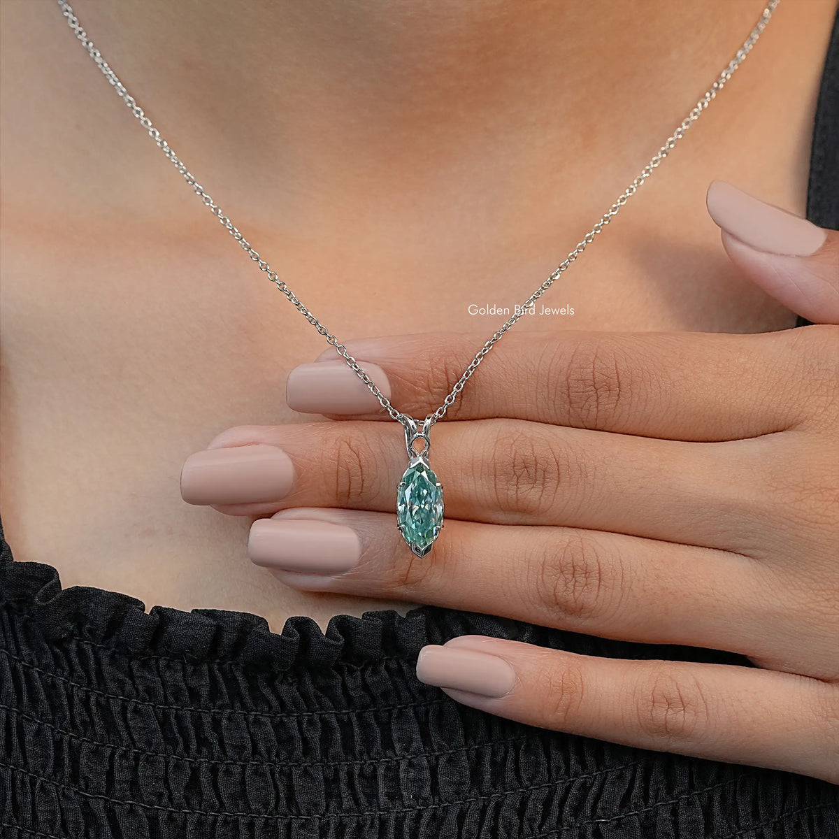 Green marquise-cut solitaire pendant on silver chain, resting on open hand with nails