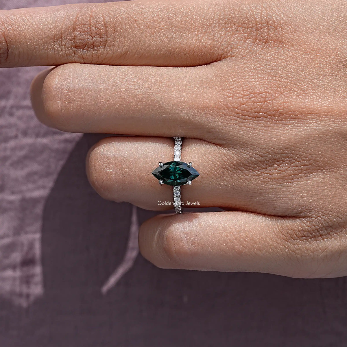 Marquise green moissanite ring on sterling silver band, side view close-up.
