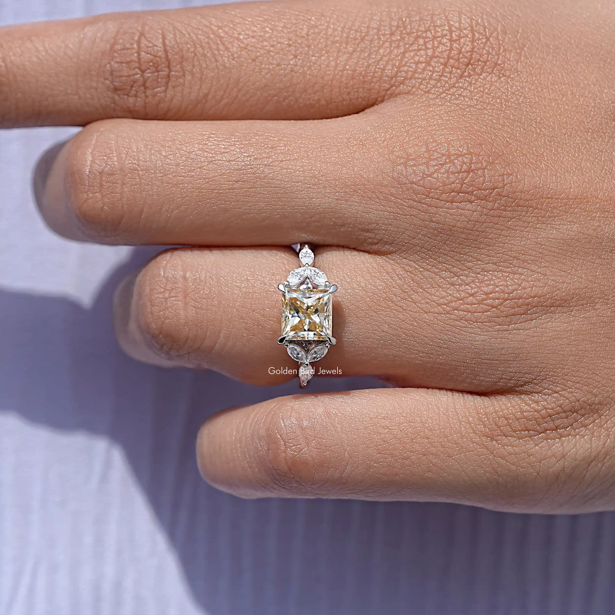 Princess-cut moissanite ring with rectangular center stone and side prongs on hand