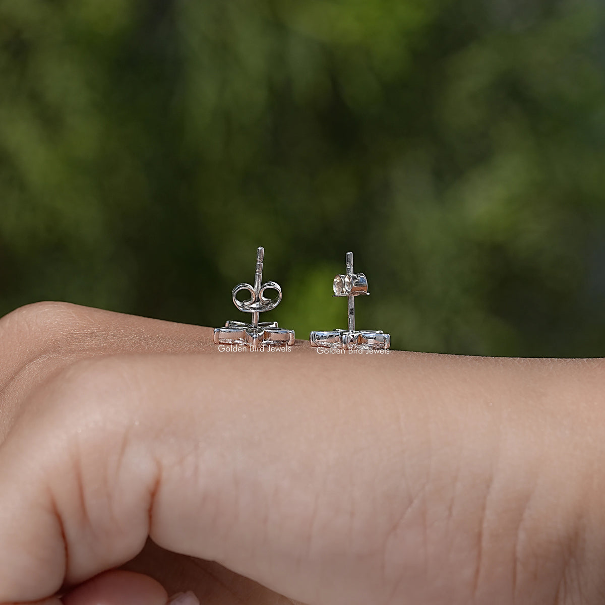 Marquise-cut diamond floral stud earrings pair on finger, silver-tone posts