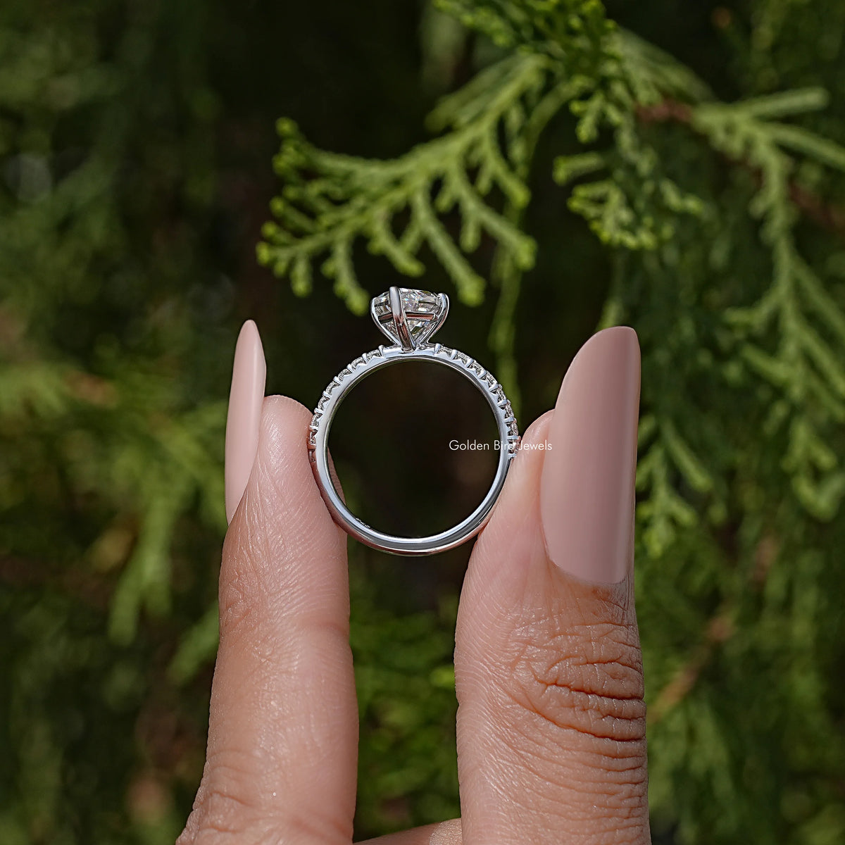 Moissanite solitaire engagement ring in sterling silver, shown between fingers.