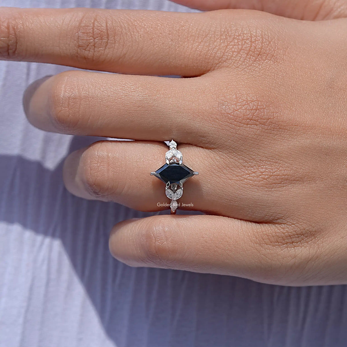 Silver ring on finger with marquise black center stone and clear leaf accents