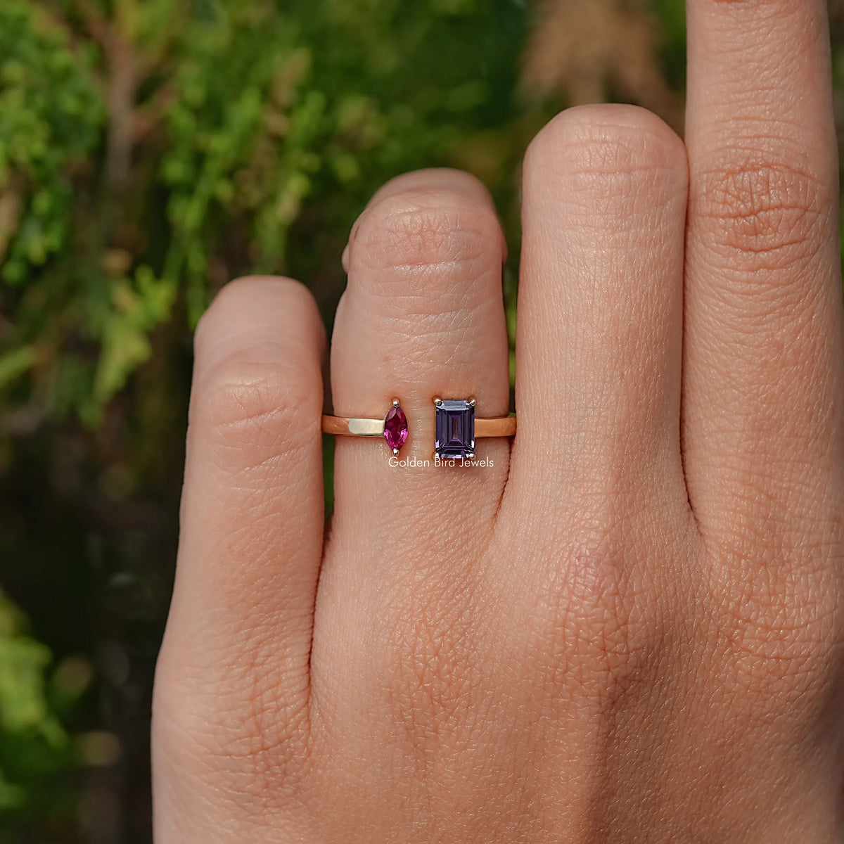 Open cuff ring on finger, marquise pink and emerald-cut dark blue stones