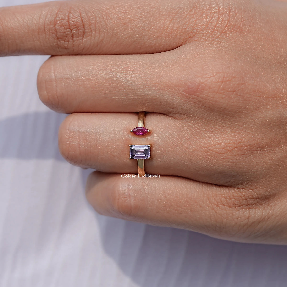 Silver-tone open cuff ring close-up on hand, marquise pink and emerald-cut dark blue stones