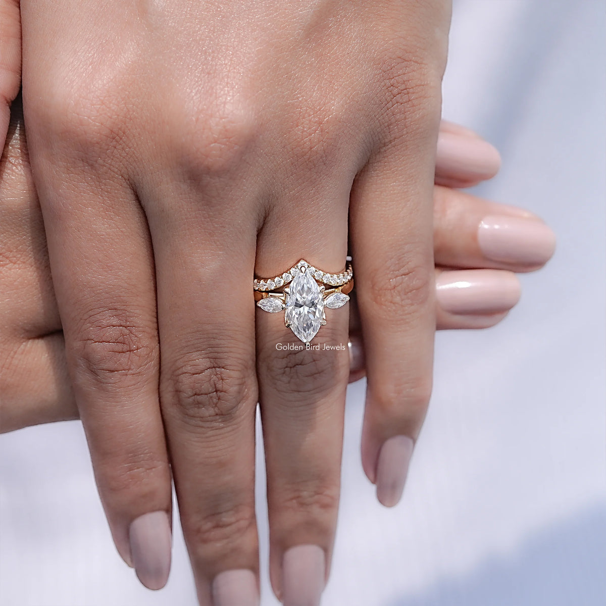 Three-stone bridal ring set with marquise-cut center stone and small side stones, stacked on hand