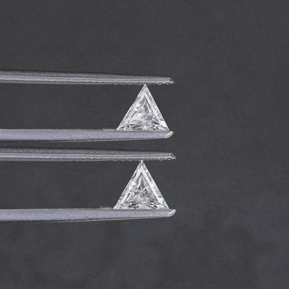 Triangle-cut clear moissanite stones held in silver tweezers, pair