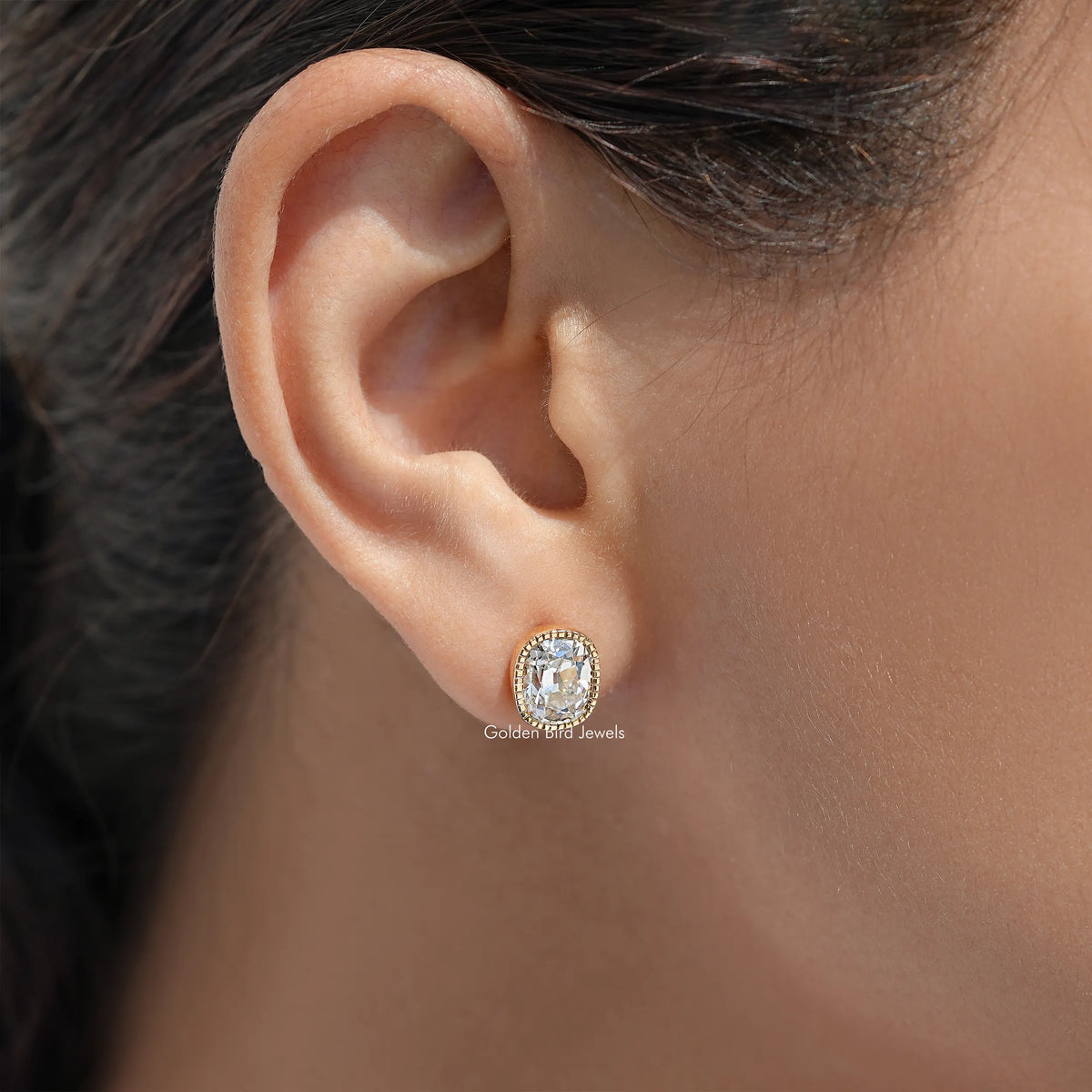 Cushion-cut diamond stud earring with milgrain bezel in gold setting on ear