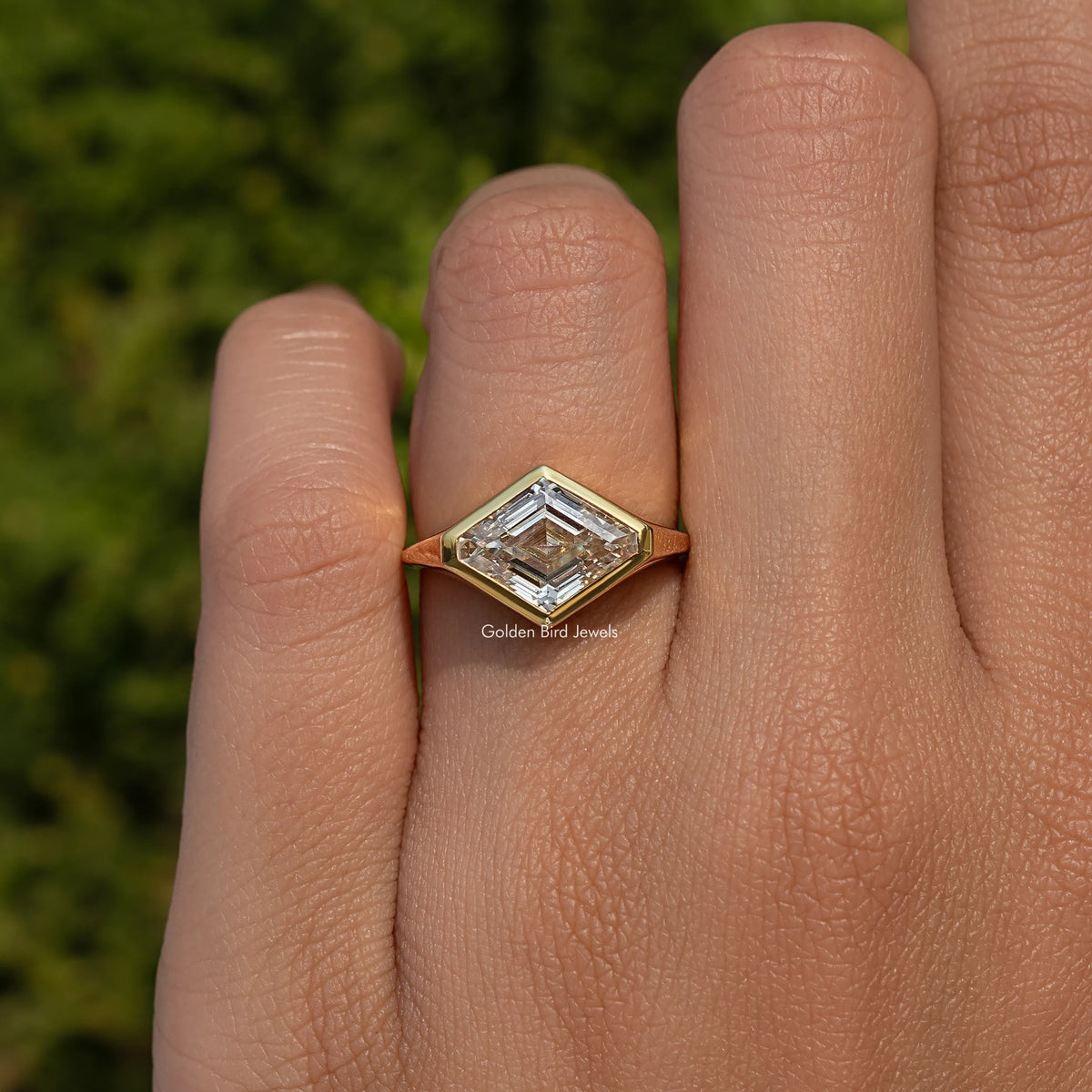 Lozenge-cut moissanite solitaire ring on hand with gold bezel setting on silver band