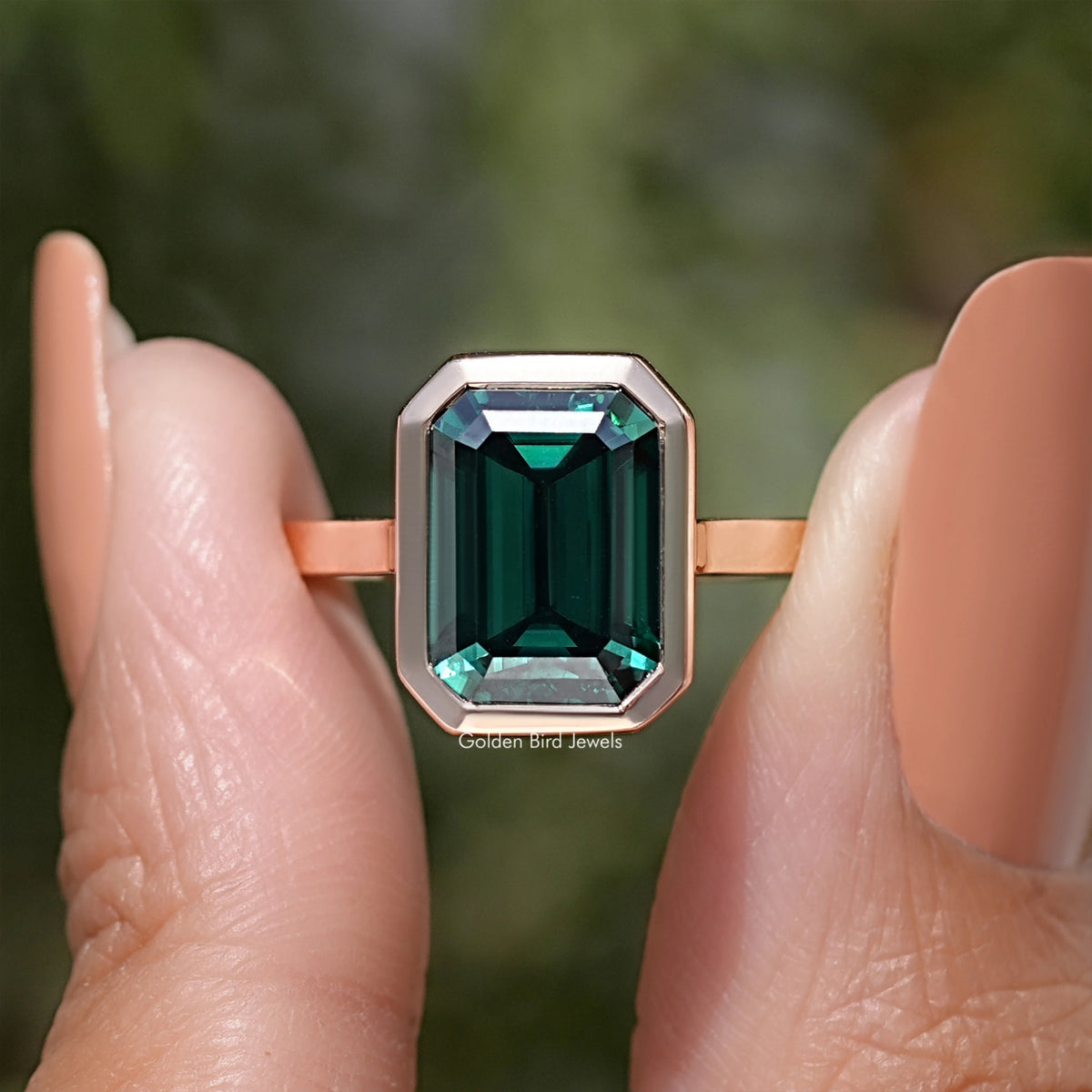 Emerald green moissanite solitaire ring with emerald-cut stone in rose gold-tone setting