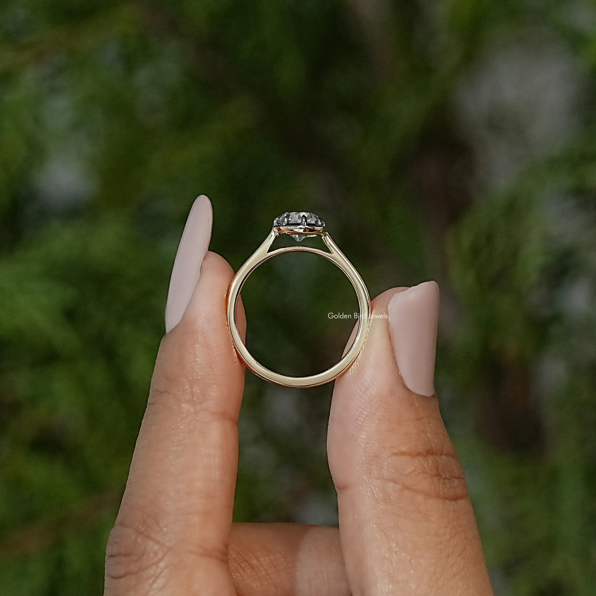 Oval moissanite solitaire ring with bezel setting, viewed from behind on gold-tone band