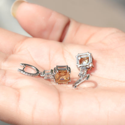 Moissanite drop earrings on palm: asscher-cut orange center with silver accents