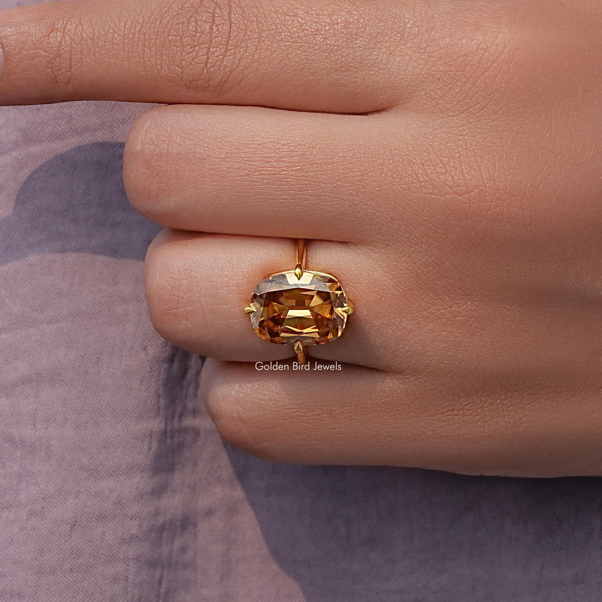 Solitaire cushion-cut moissanite ring with golden center stone on a gold band, close-up