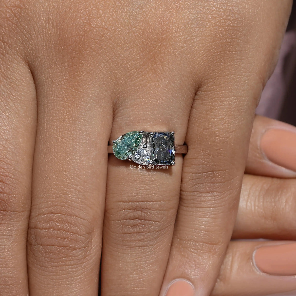 Three-stone moissanite ring on finger, oval green center with two dark side stones