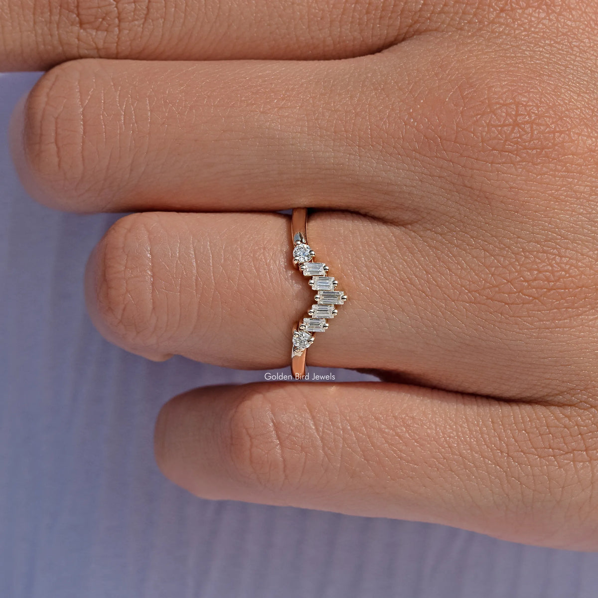 Curved wedding band ring with staggered baguette-cut stone row, close-up on finger