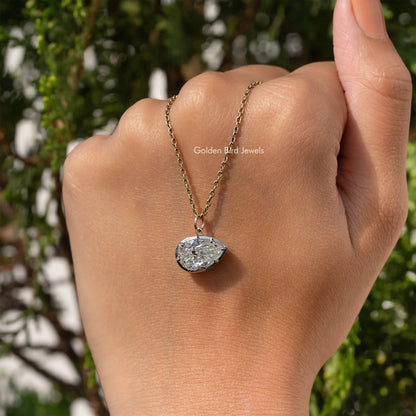 Gold-tone pear-shaped pendant on fine chain on hand, bezel-set moissanite