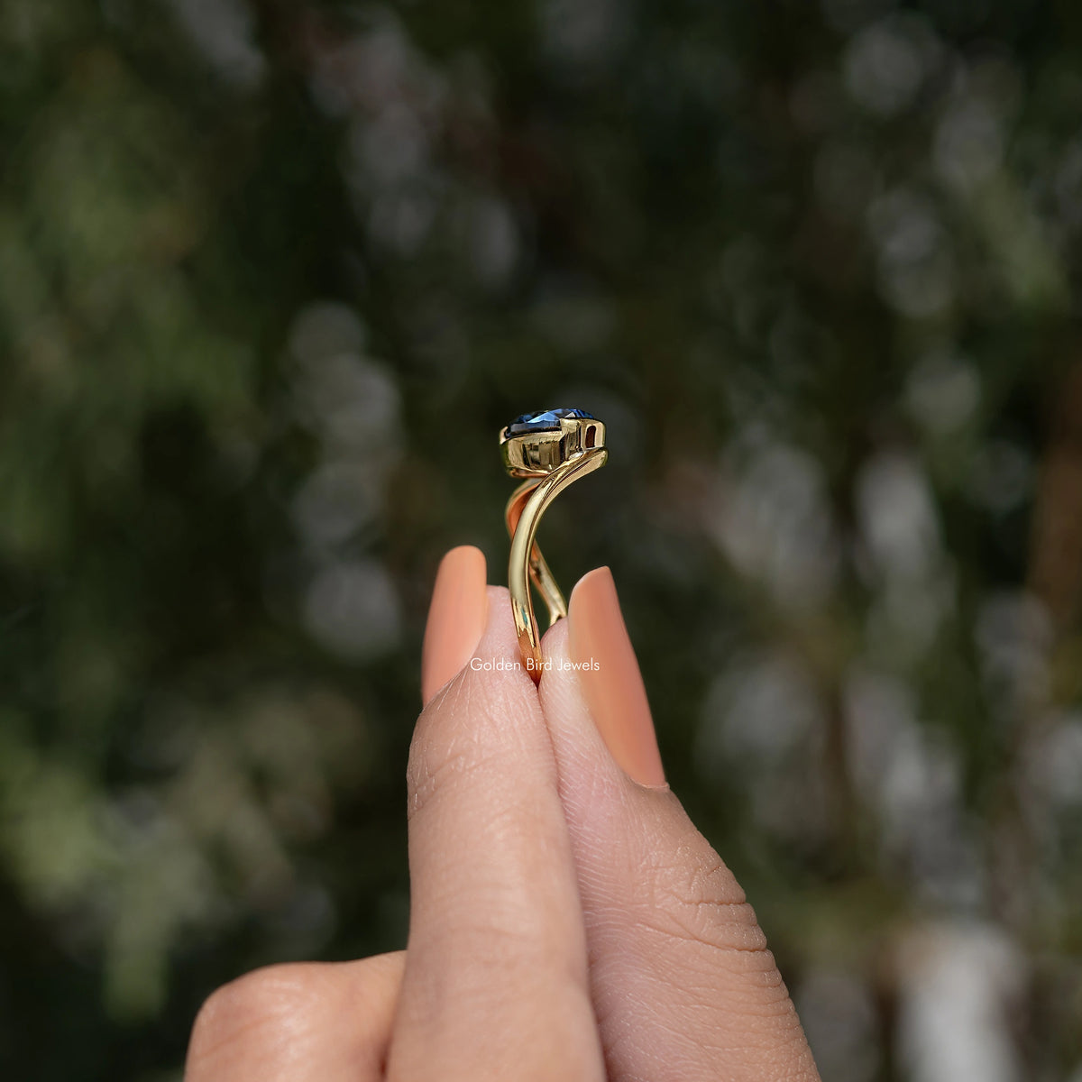 Curved solitaire ring with blue pear-cut gemstone in gold setting