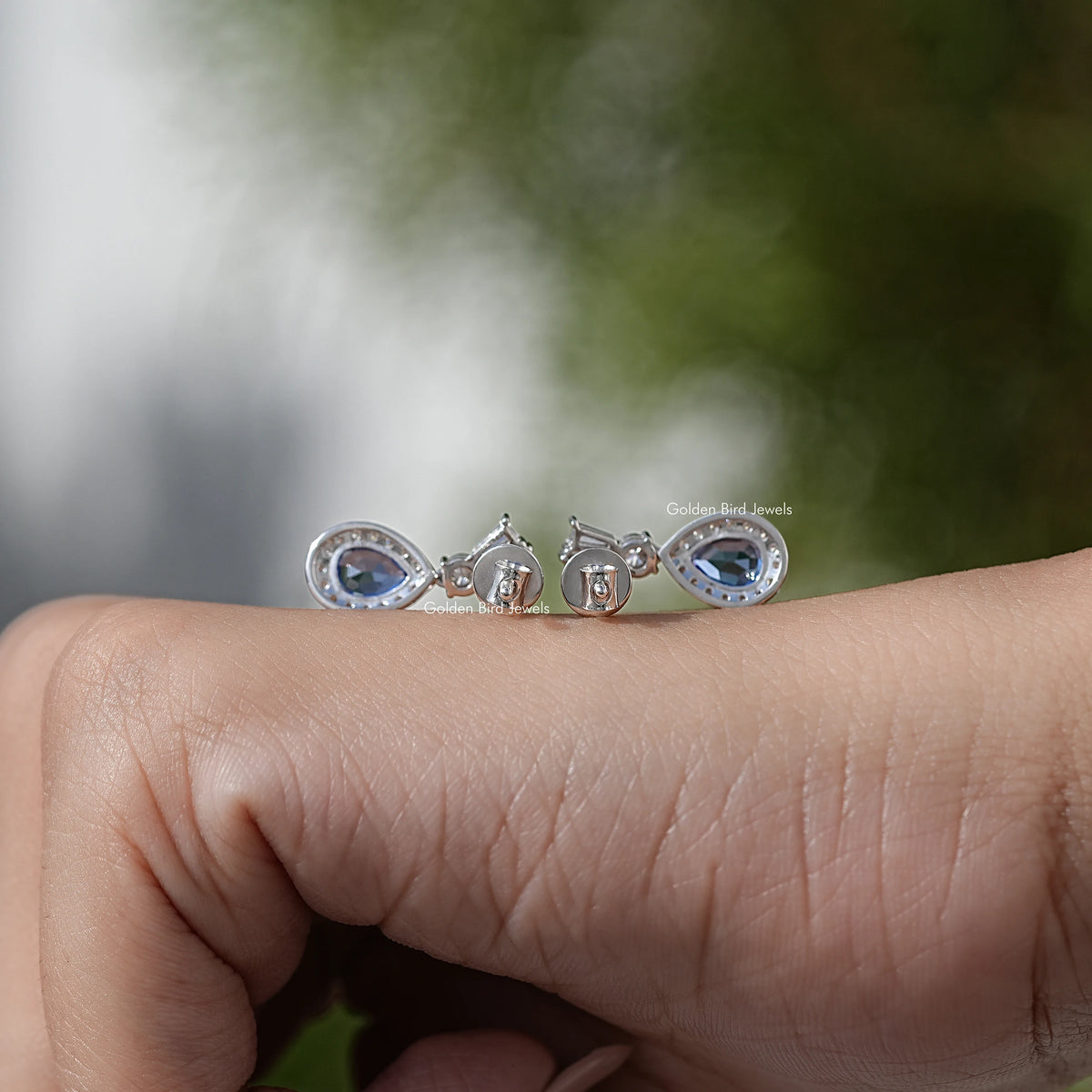 Silver-tone blue pear-cut halo dangle earrings, full set view on open hand