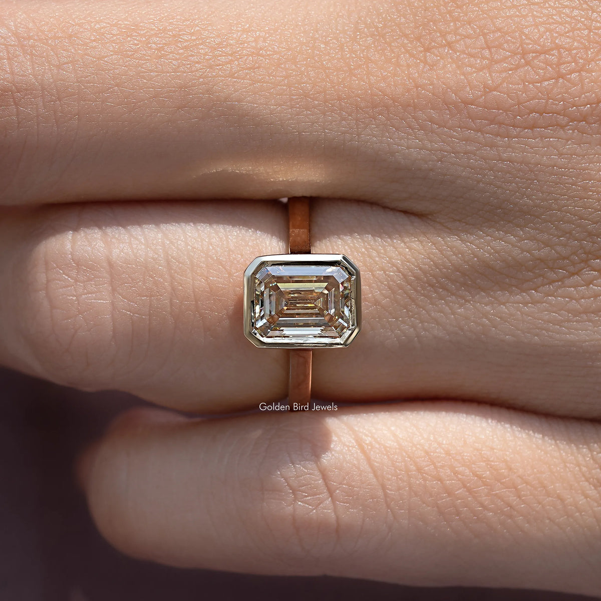 Emerald-cut solitaire stone centerpiece on rose-gold band, close-up view