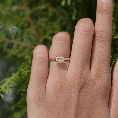 Oval cut moissanite solitaire ring on finger, four-prong crown.