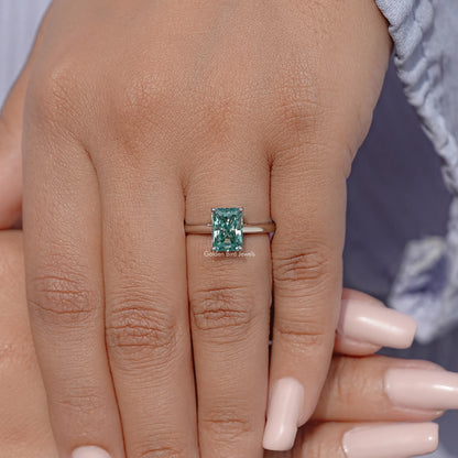 Sterling silver solitaire engagement ring with emerald-cut blue-green moissanite on hand.