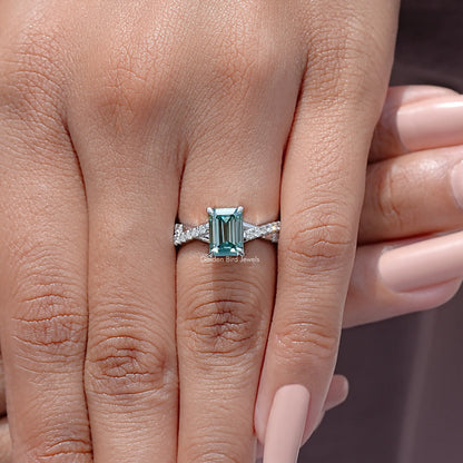 Emerald-cut teal moissanite ring with twisted silver band, worn on hand
