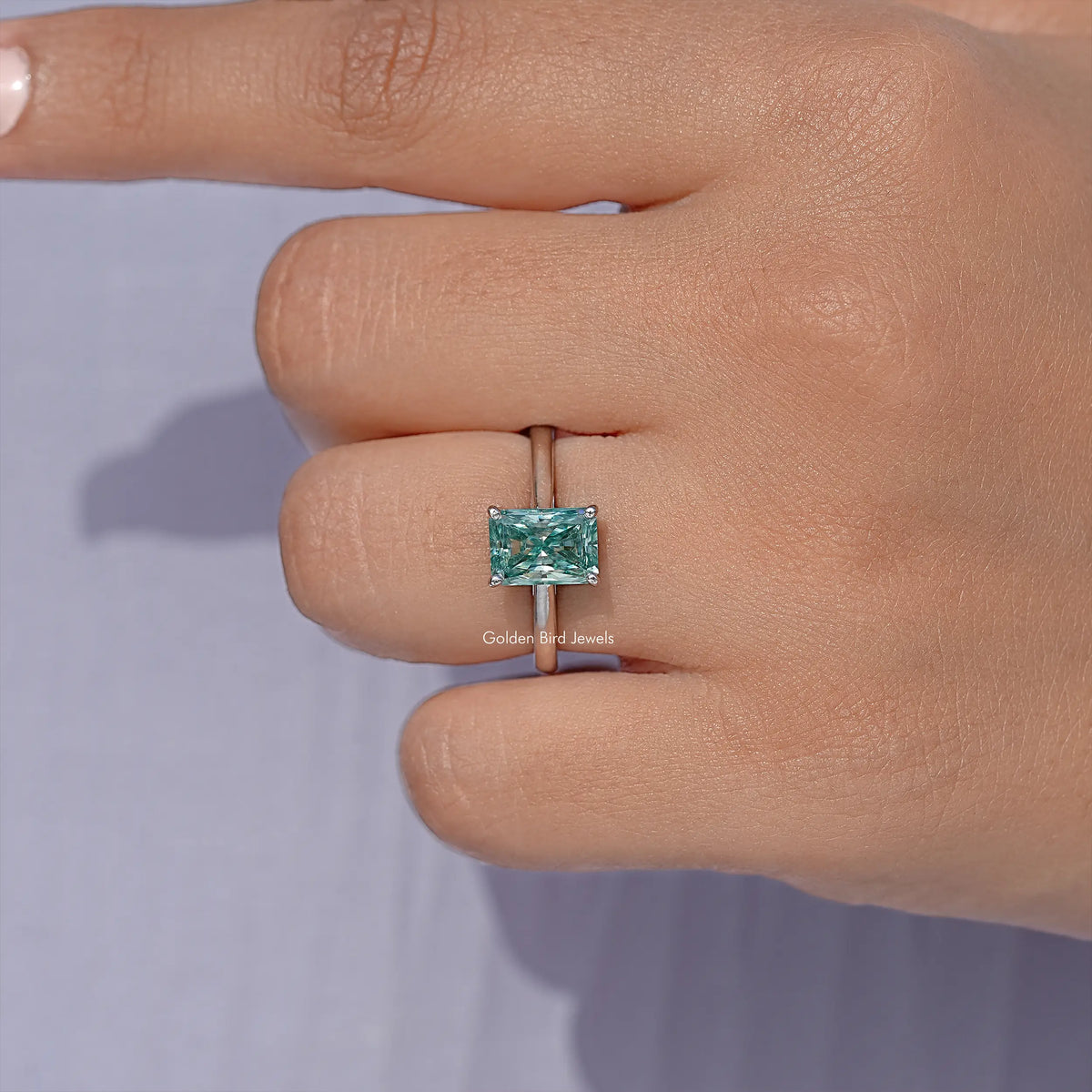 Emerald-cut blue-green moissanite solitaire ring in sterling silver, close-up.