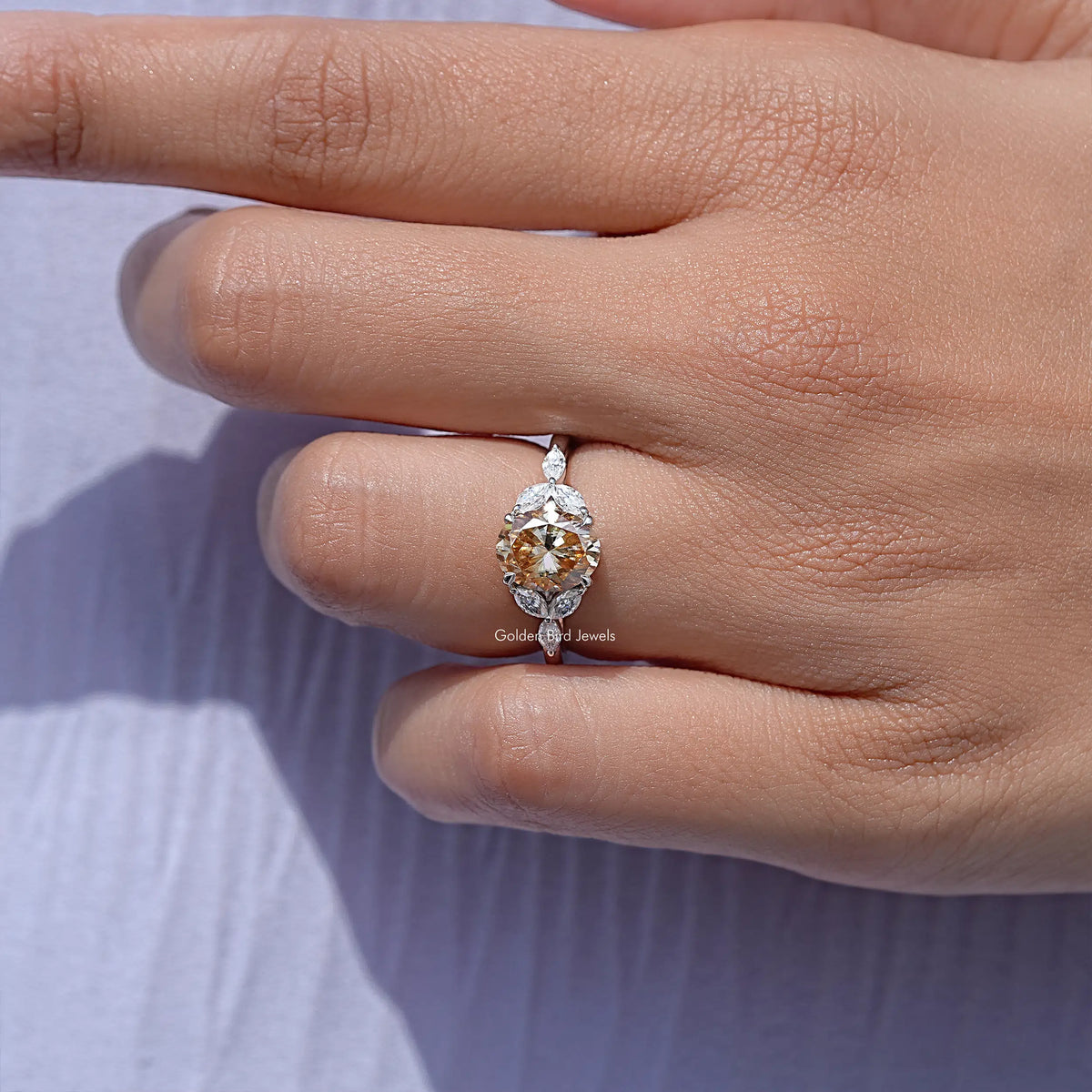 Oval moissanite ring with leaf side stones, center stone tilted in hand close-up