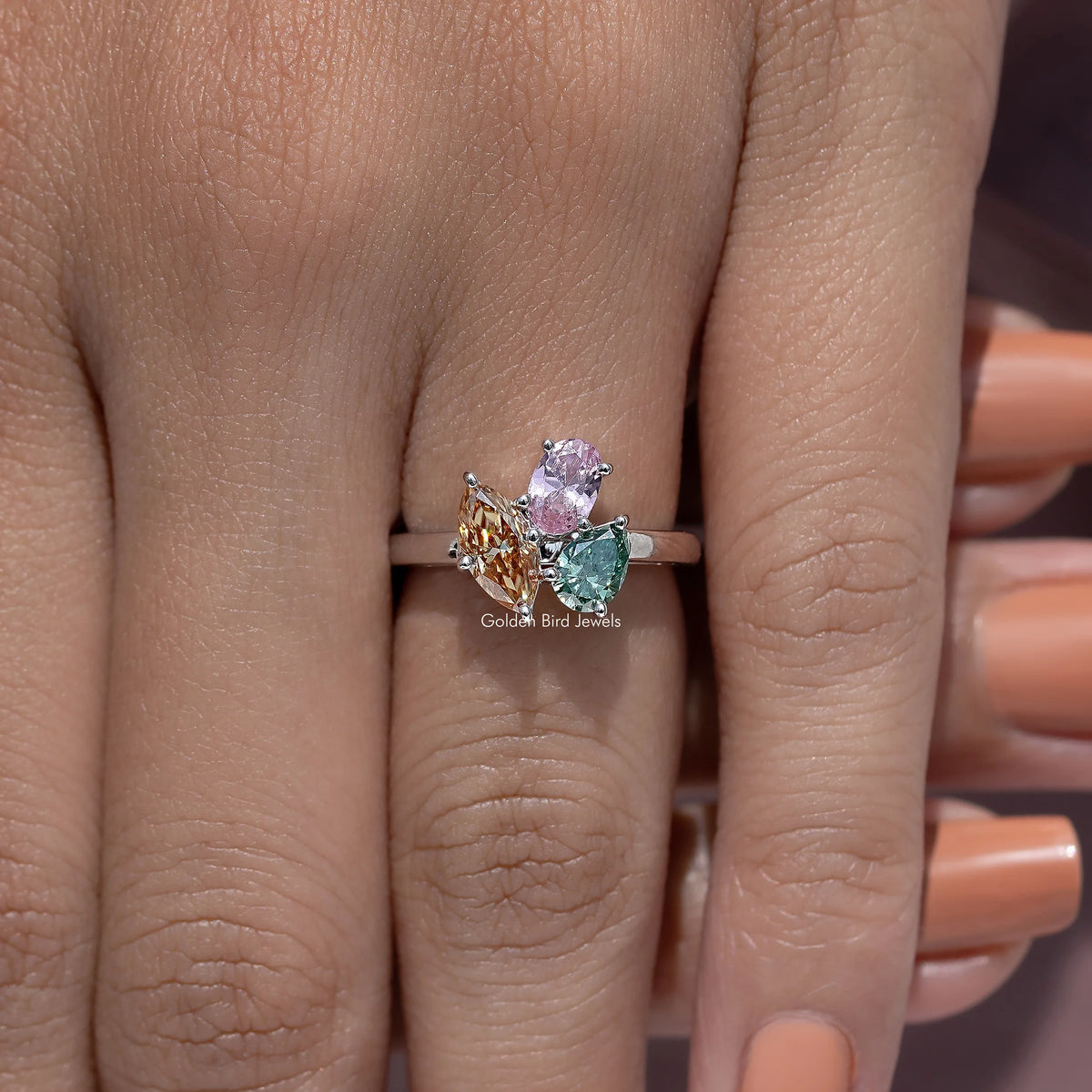 Three-stone engagement ring with green and pink stones plus an amber center gem