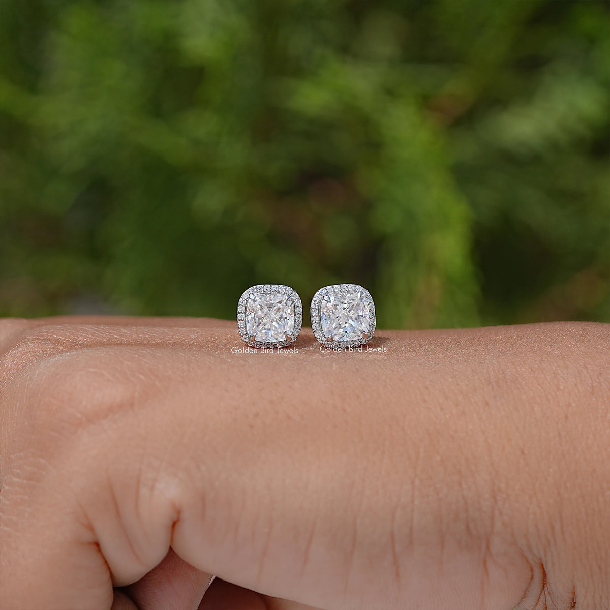 Pair of cushion-cut halo stud earrings resting on wrist