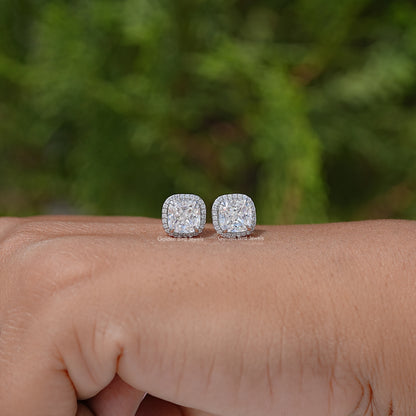 Pair of cushion-cut halo stud earrings resting on wrist
