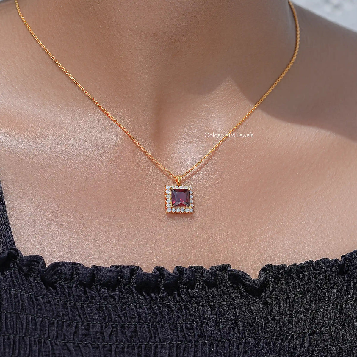 Square ruby-red gemstone pendant with halo detail on gold chain necklace