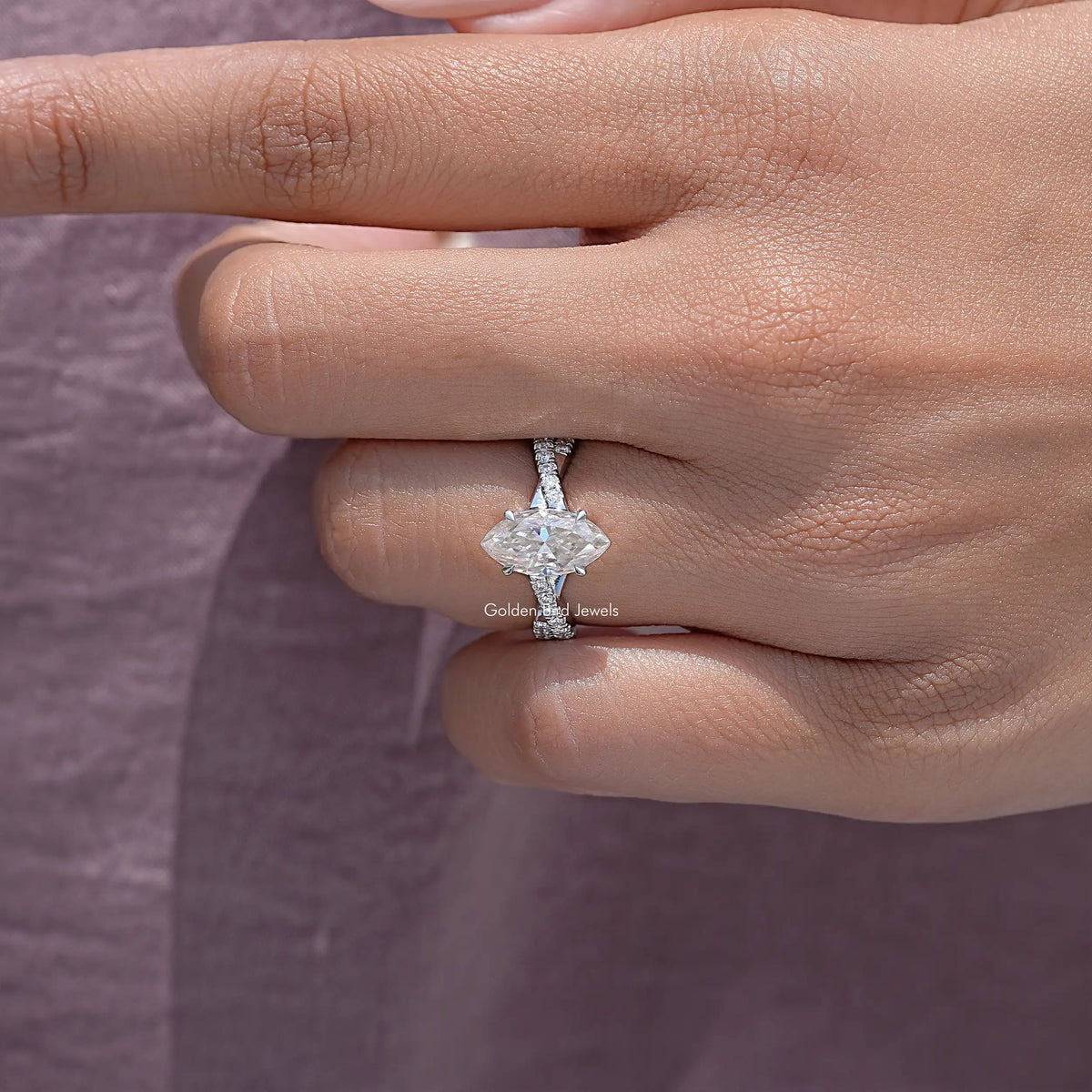 Twisted accent wedding ring close-up on fingertips; marquise center stone