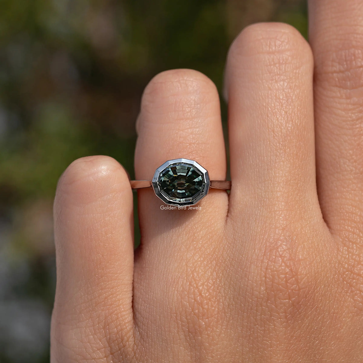 Bezel-set solitaire ring featuring dark green step-cut stone on the finger