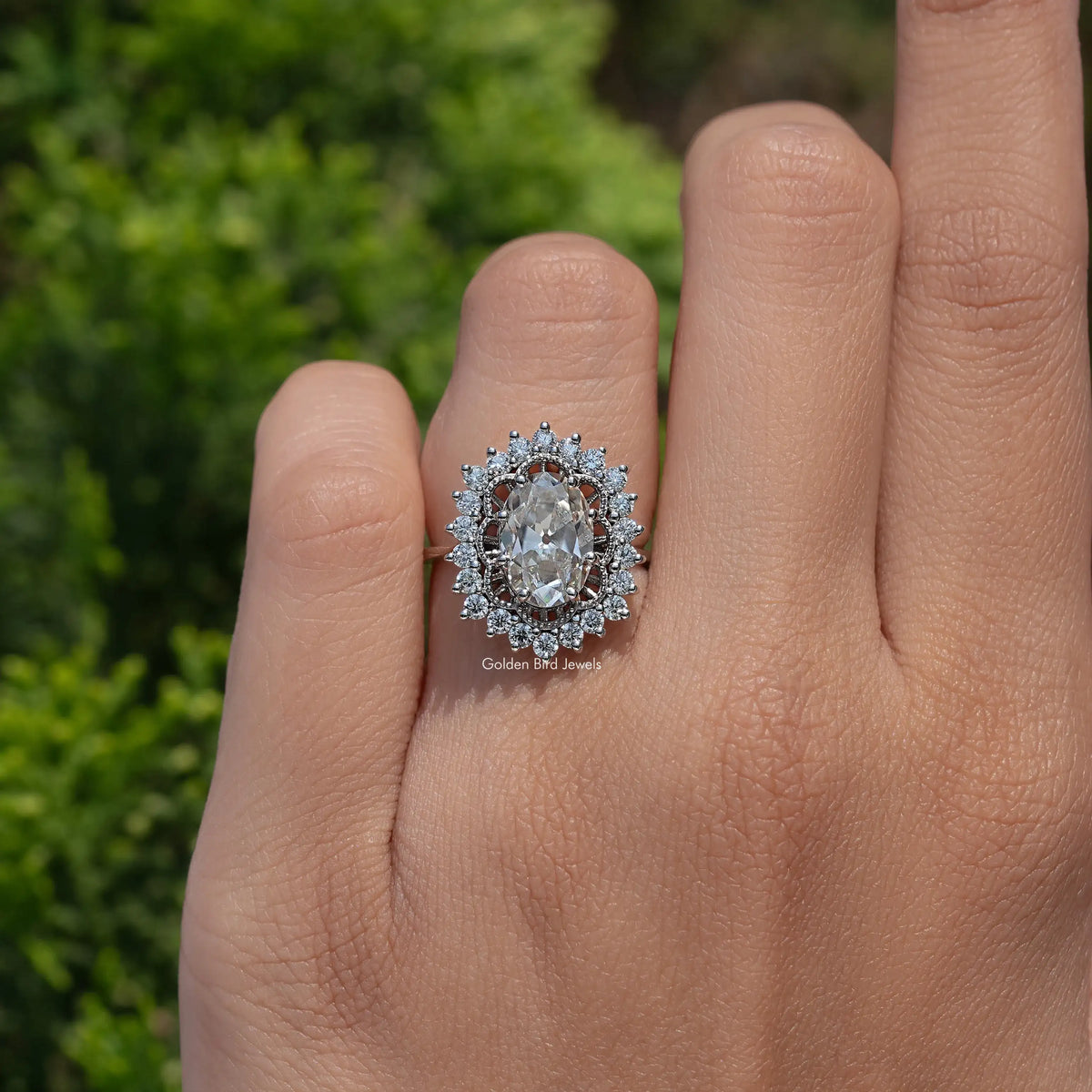 Oval moissanite halo ring with detailed halo and split shank, close-up on hand