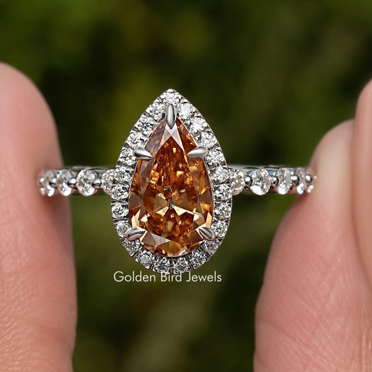 Moissanite pear-cut halo engagement ring with orange center stone and pavé band