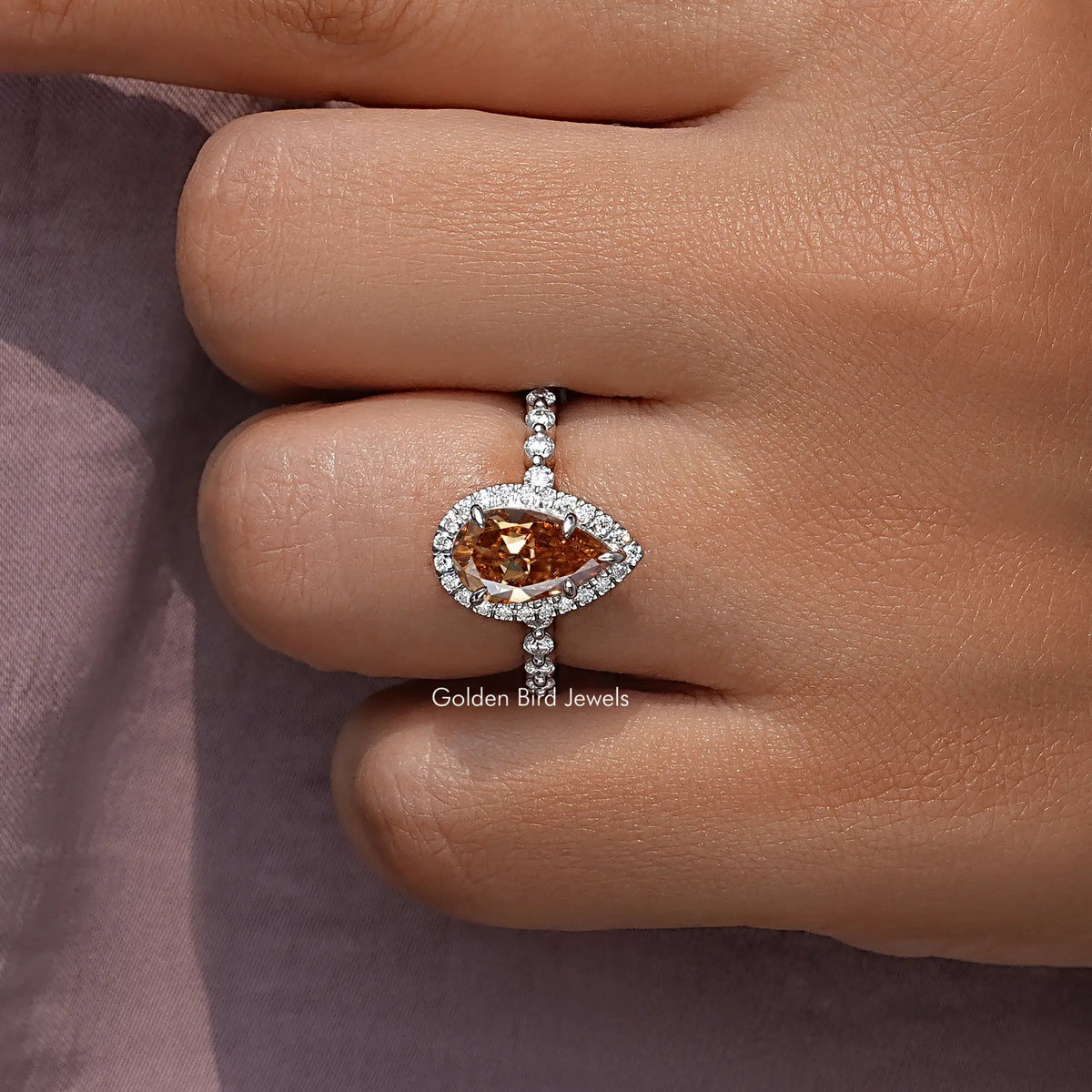 Pear-shaped warm orange center stone in 925 sterling silver halo with vertical side stones