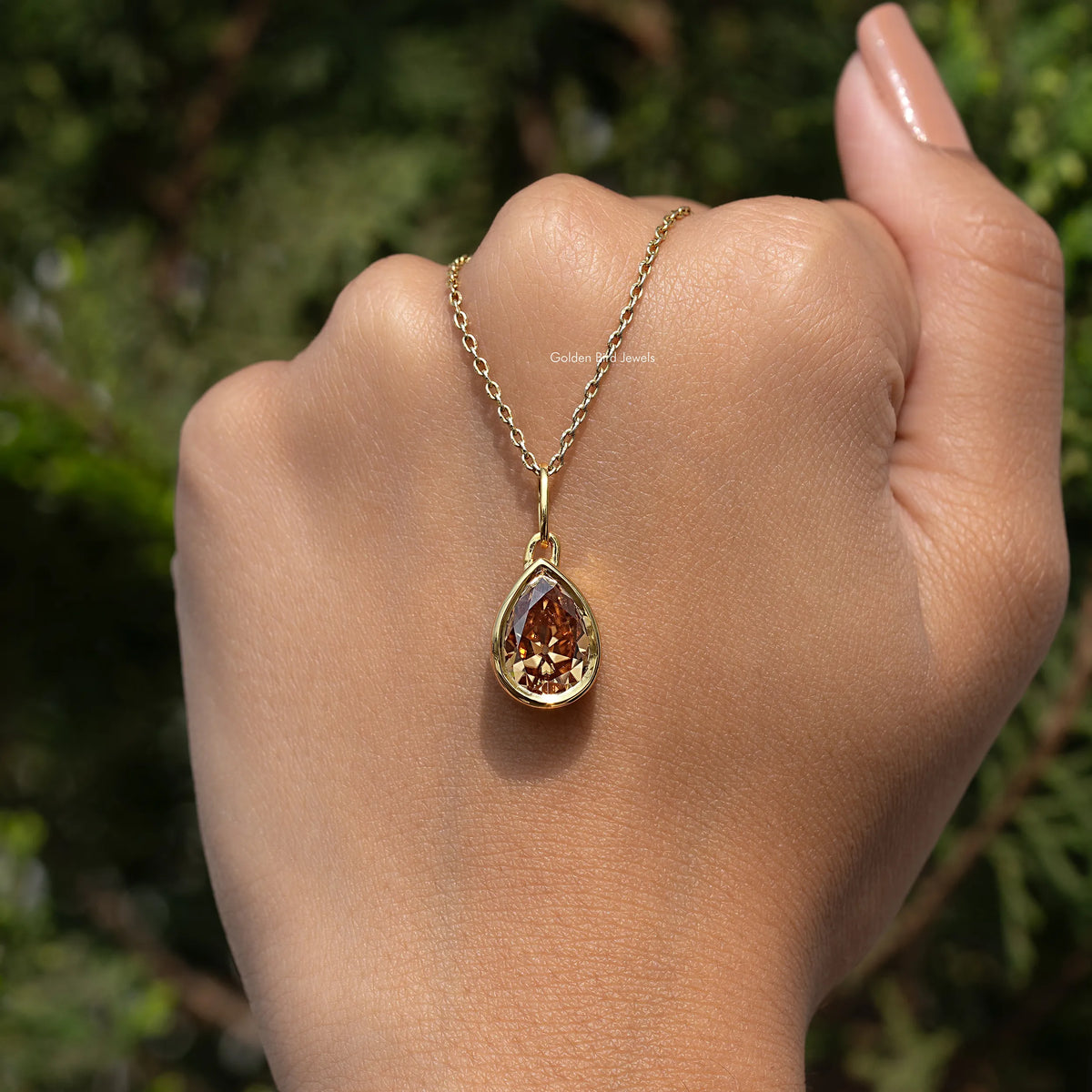 Gold teardrop pendant necklace with champagne-colored pear-cut gemstone on palm