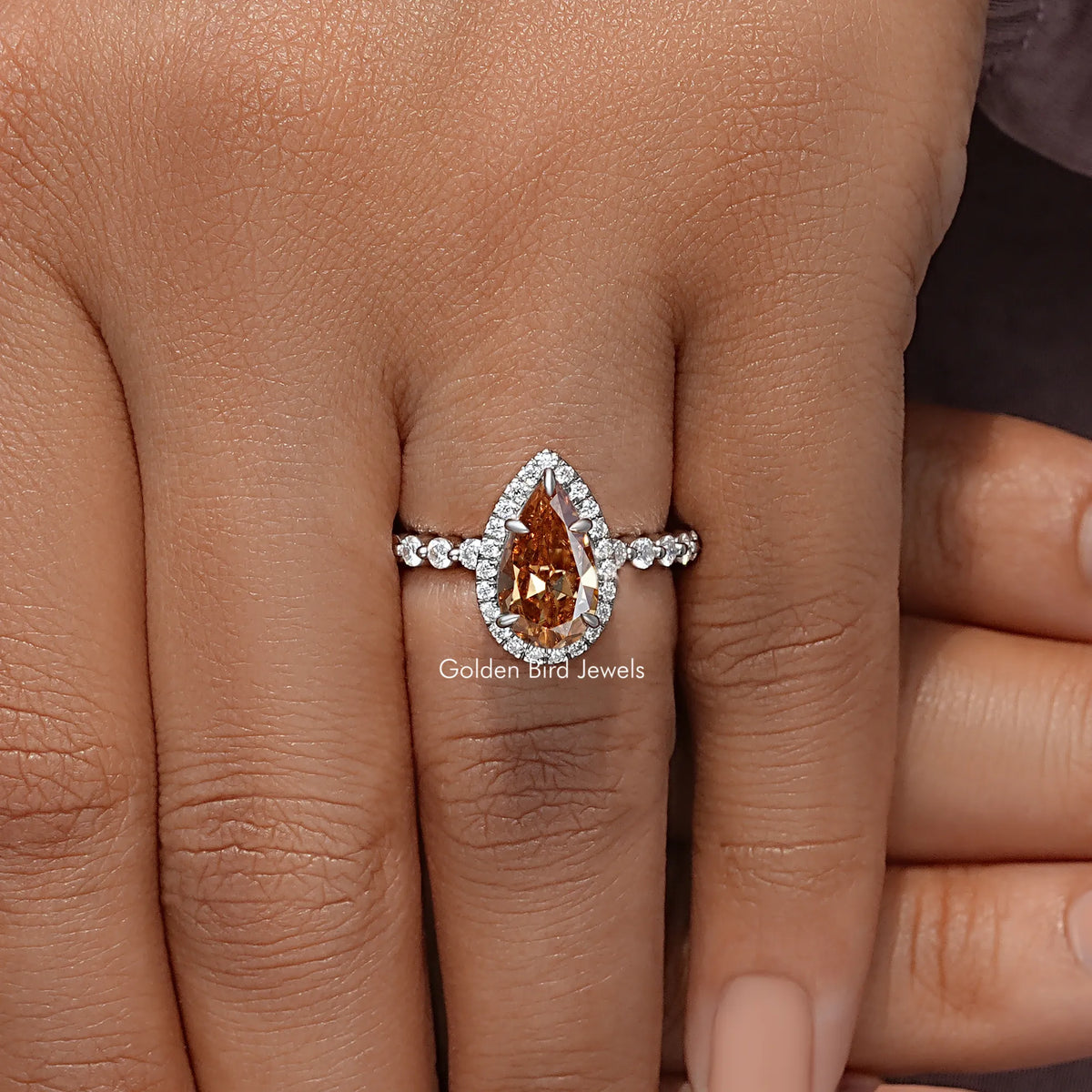 Pear-cut halo engagement ring on hand with orange teardrop center and diamond band