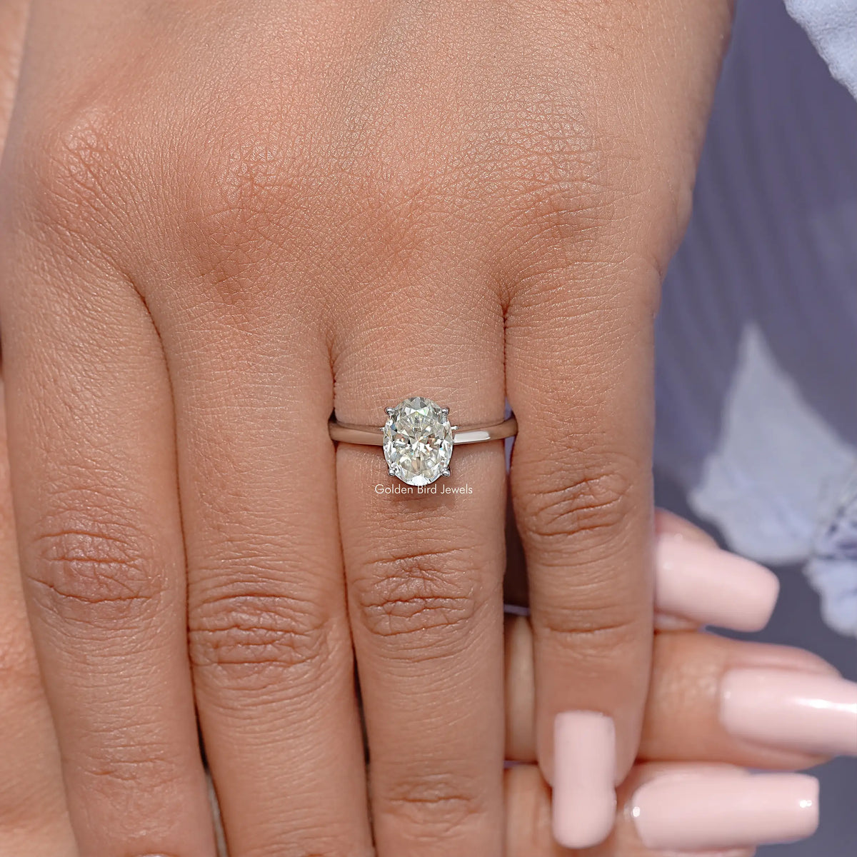 Oval moissanite solitaire ring with prong-set oval stone on finger, slim silver band