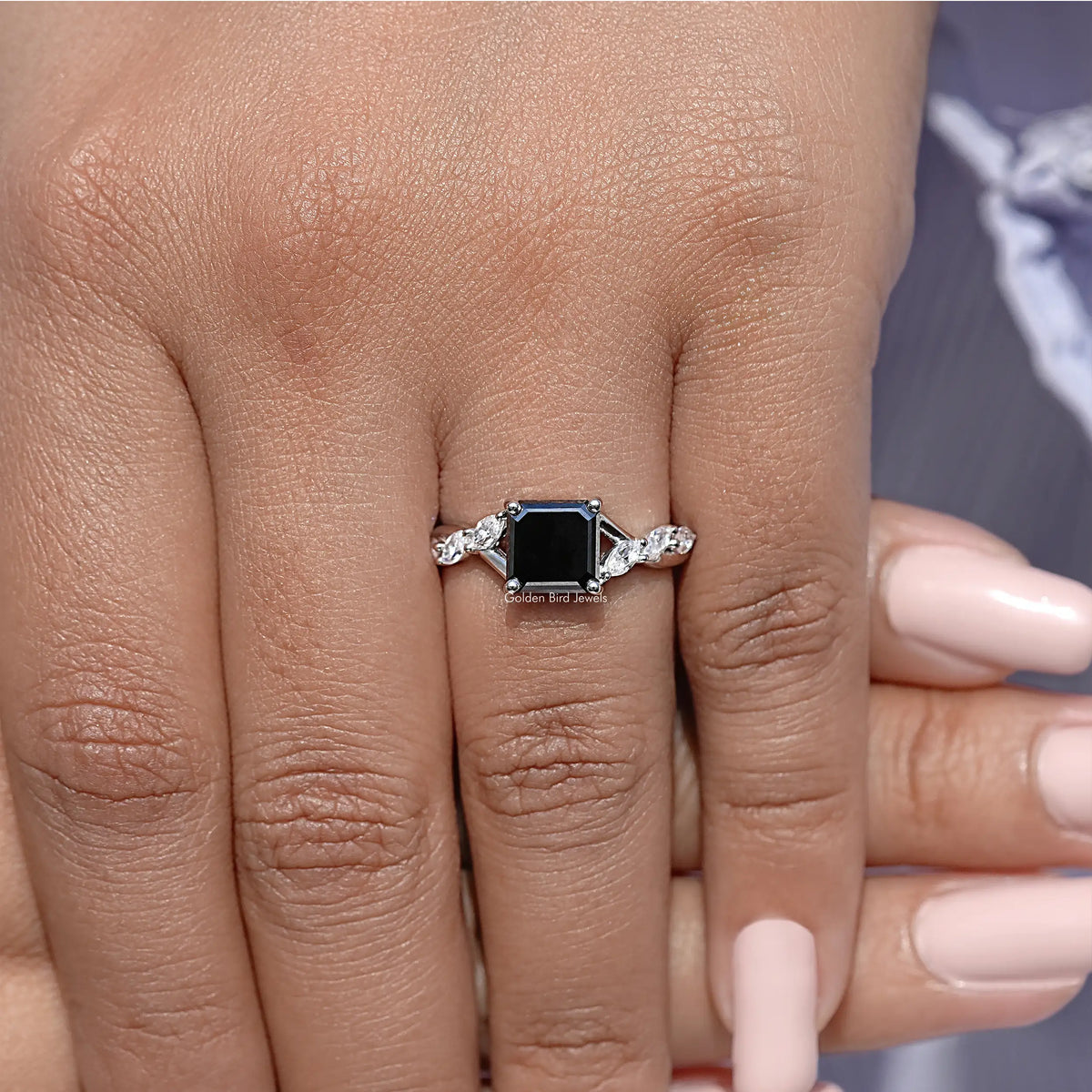 Asscher-cut black center ring on finger with halo stones flanked by round accents