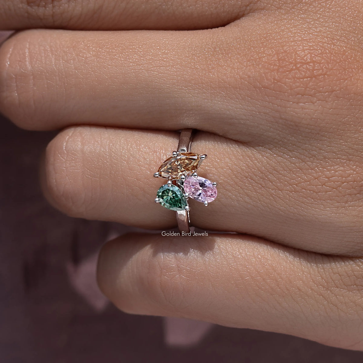 Three-stone engagement ring with green, pink, and clear prong-set gemstones