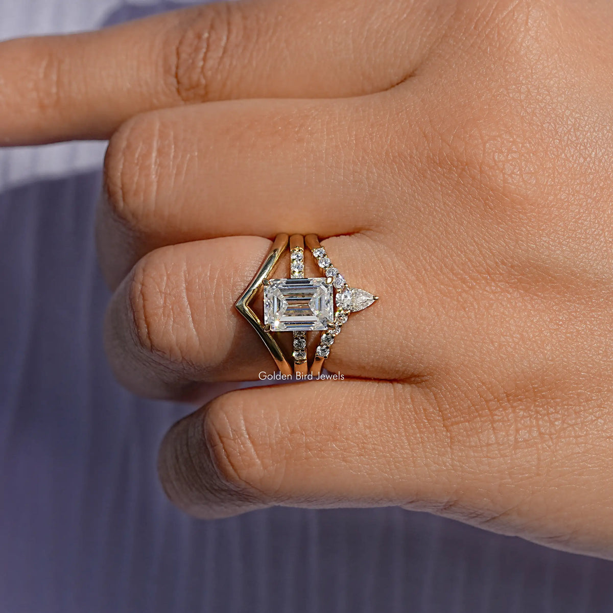Three-stone bridal ring on finger, gold-toned setting with rectangular center stone