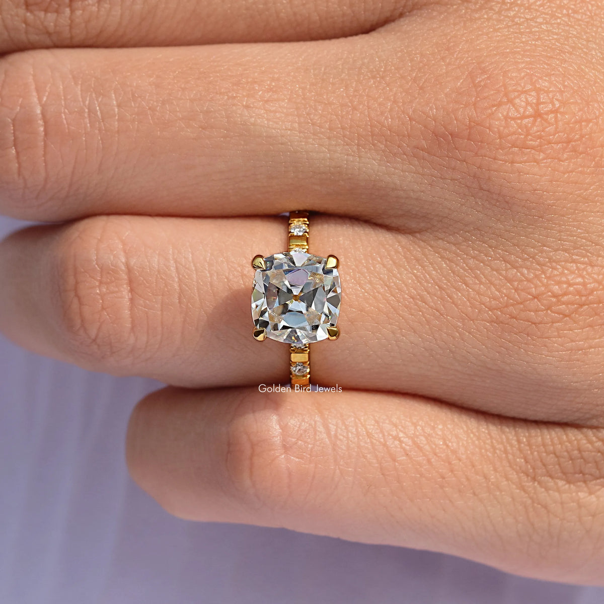 Gold-tone ring on finger, cushion-cut moissanite center with channel-set side stones