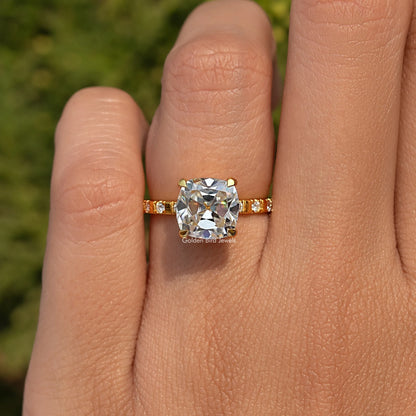 Gold-tone ring with cushion-cut moissanite center stone and small side accent stones